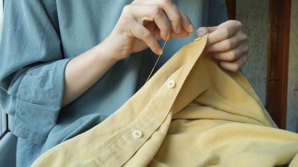 Close up woman's hands sewing a button to a yellow shirt. Female at work