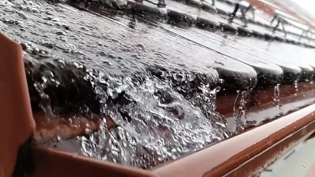 Close up of water falling down to gutter from the roof during heavy rain storm, slow motion footage clip.