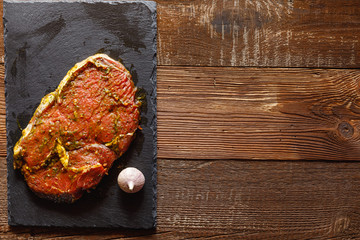 slice of raw meat on slate slab with garlic on wooden table