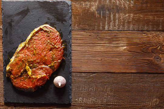 slice of raw meat on slate slab with garlic on wooden table