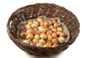 Rustic vine basket filled with yellow onions lying on a linen bag, view from the side. Isolated object. Vegetable background. Concept of food, farm products.