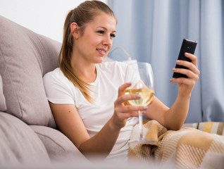 Positive woman sitting on sofa with wineglass and chatting on phone