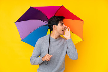 Man holding an umbrella over isolated yellow background shouting with mouth wide open