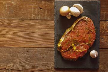 Slice of spiced raw beef on slate plate with garlic and mushroom on wooden table