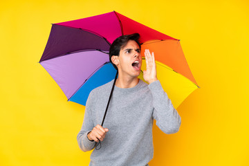 Man holding an umbrella over isolated yellow background shouting with mouth wide open