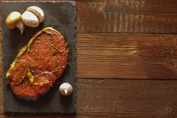Slice of raw beef on slate plate with garlic and mushroom on wooden table