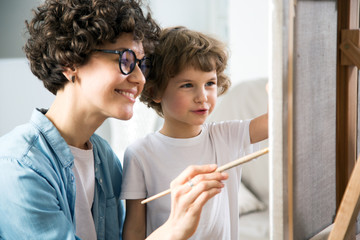 Happy mother and baby son drawing together on a easel
