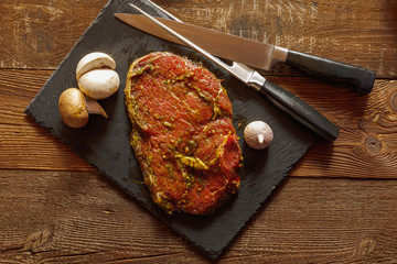 Slice of spiced raw beef with garlic and mushroom on slate plate with meat knife and fork on wooden table
