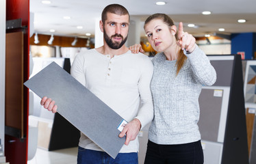 Young family couple standing with sample of ceramic tile in shop