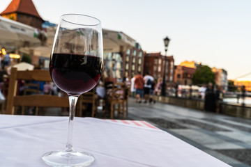 A red wine glass kept on a white table before blurred Gdansk city center main square located in North Poland near baltic sea