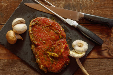 Slice of spiced raw beef with garlic and mushroom on slate plate with meat knife and fork on wooden table