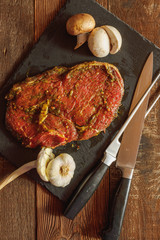 Slice of spiced raw beef with garlic and mushroom on slate plate with meat knife and fork on wooden table