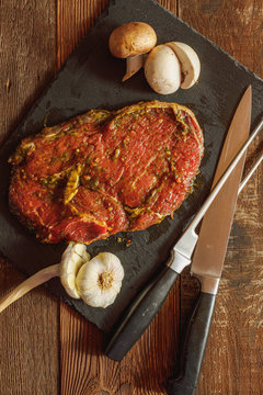 Slice of spiced raw beef with garlic and mushroom on slate plate with meat knife and fork on wooden table
