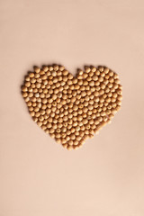 Pile of kabuli chickpeas in shape of heart on beige, light tan background. Heap of  legumes bean seeds grains, top view. Ingridient for hummus, falafel. East Asian traditional cuisines. Healthy food.