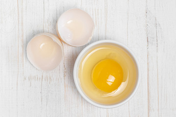 Row fresh egg in ceramic small white plate and two parts of shell above view on painted wooden background  macro
