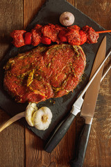 Slice of spiced beef with bbq skewer of beef and tomato with garlic knife and fork on slate plate on wooden table