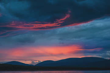 Beautiful mystical sundown in hills with dramatic clouds and reflection in the water