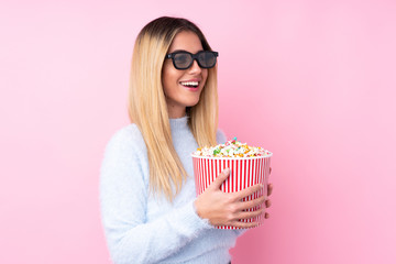 Young Uruguayan woman over isolated pink background with 3d glasses and holding a big bucket of popcorns