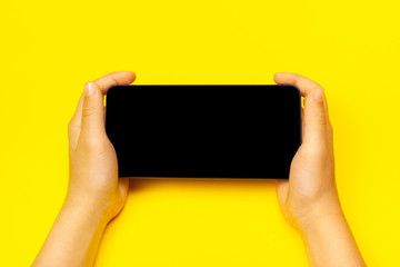 Smart phone with child's hands on the yellow backstage. The concept of necessary things of a little girl, technology for children. Flat lay, copy space.