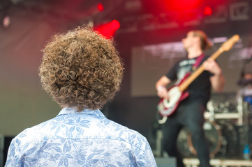 a curly haired person watching a live band at a music concert