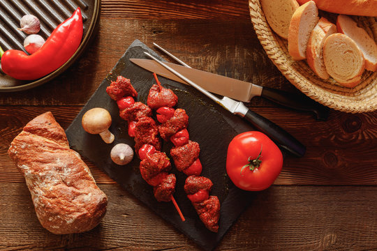 bbq skewer of beef and tomato on slate plate with garlic and mushroom bread in basket chilli pepper and cast-iron grill pan