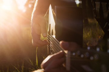 Musician playing guitar in nature. Soft selective focus on fingers and strings.