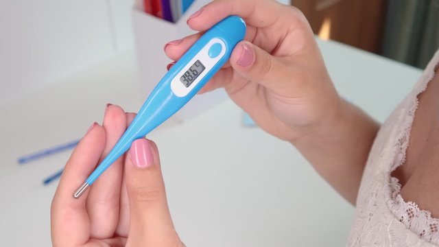 The girl holds a thermometer in her hands. High temperature is a symptom of a viral disease.