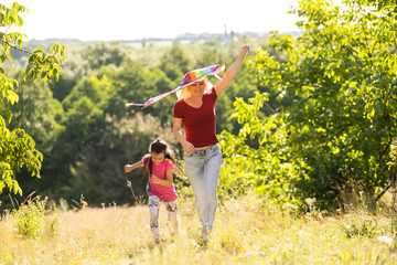 happy family mother and child run on meadow with a kite in the summer on the nature