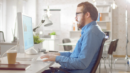 Young Bearded Hipster Man Working on Personal Computer while Sitting in His Bright Modern Creative Agency Office.