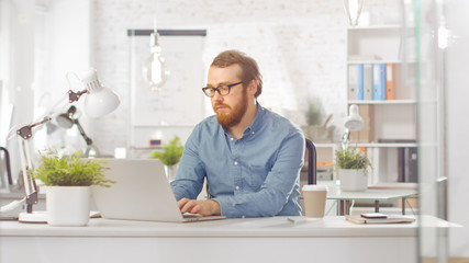 Shot of a Focused Young Creative Guy Using Laptop, Typing. He is working in a Bright Modern Loft Office.