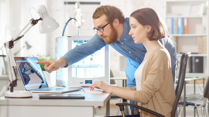 Fototapeta premium Shot of a Young Bearded Male Manager Gives Advice to a Female 3D Engineer, who is using Laptop Computer. Bright Modern Office with Programmable 3D Printer.