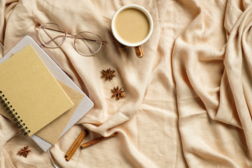 Autumn flatlay composition. Paper notebook, glasses, coffee cup on beige plaid. Autumn hygge style desk table or winter holiday concept.
