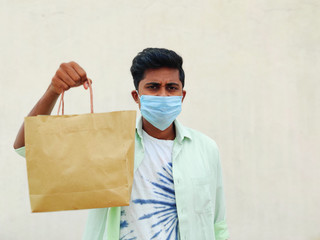 Young South Indian wearing mask is holding shopping bag. Isolated on white background. Shopping concept in corona virus period.