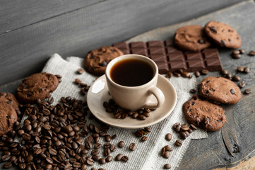 Coffee cup with cookies and chocolate with scattered coffee beans on linen and wooden table background. Mug of black coffee.