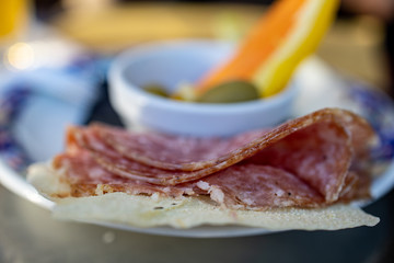Selective focus. Individual snack plates in cocktail bar in Milano during the typical evening aperitif: chunks of pizza or focaccia, slices of salami, olives and thinly sliced veggies.