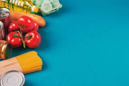 Top view on food donations on green background with copyspace - pasta, fresh vegatables, canned food, baguette, eggs, organic oil. Donation, volunteering or contactless delivery food concept. Flat lay