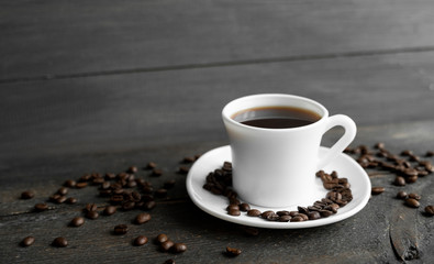 Coffee cup with roasted coffee beans on wooden table background. Mug of black coffe with scattered coffee beans on a wooden table. Fresh coffee beans.