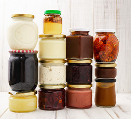 Various jars with canned vegetables, oils on a light wooden background.