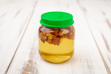 Walnut with honey in a glass jar on a light wooden background.