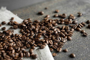 Coffee beans on a linen textile and on a wooden table background. Fresh arabica coffee beans.