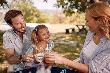 Parents with  daughter sitting at table outdoor and  enjoying together.
