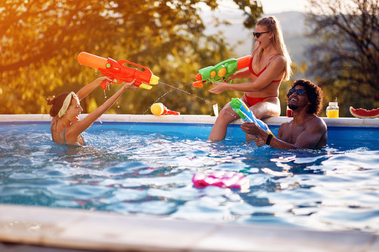 People on pool party, celebration summer vacation.Friends having fun with water guns in pool