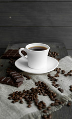 Coffee cup with cookies and chocolate with scattered coffee beans on linen and wooden table background. Mug of black coffee.