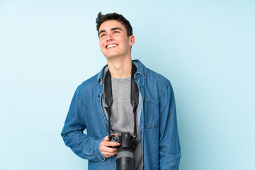 Teenager photographer man isolated on blue background laughing and looking up