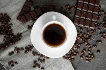 Coffee cup with cookies and chocolate with scattered coffee beans on linen and wooden table background. Mug of black coffee.
