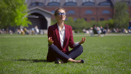 Fototapeta premium Beautiful businesswoman calming and meditating on grass in summer park