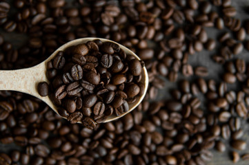 Fresh roasted arabica coffee beans in a wooden spoon and scattered coffee beans on a wooden table.