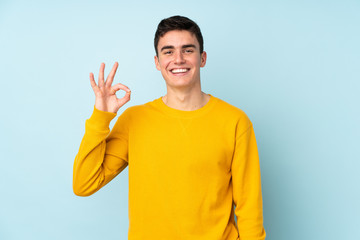 Teenager caucasian handsome man isolated on purple background showing ok sign with fingers