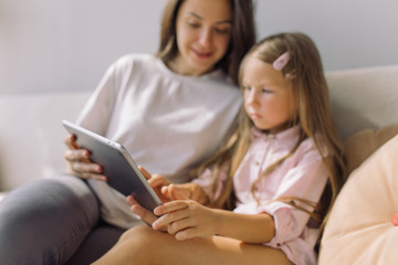 Nanny showing educational cartoon on tablet to little girl. Focus on technology.