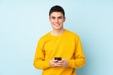 Teenager caucasian handsome man isolated on purple background sending a message with the mobile